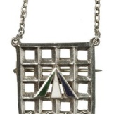 Holloway brooch designed by Sylvia Pankhurst. Comprising a porcullis symbol of the House of commons, the gate and hanging chaines in silver and the superimposed broad arrow in purple, white and green enamel. Referred to in Votes for Women, 16 April 1909 and first presented to ex-suffragette prisoners at a mass demonstration at the Albert Hall on 29th April 1909.
